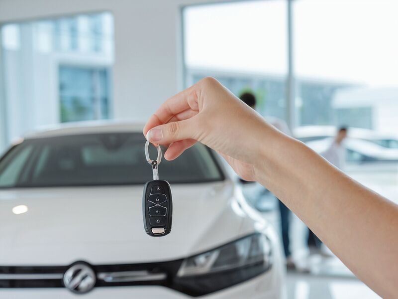 A hand holding a set of new car keys in front of a car in a showroom